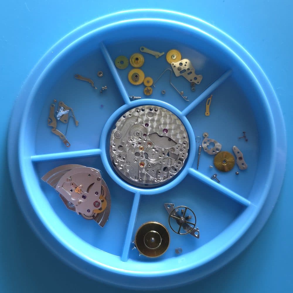 A watch movement fully disassembled into a parts tray during a service overhaul